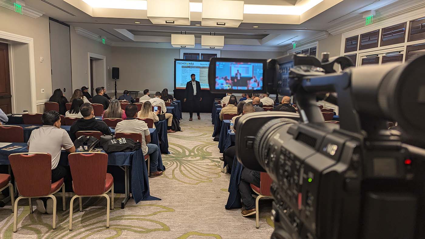 view from behind a video camera of a webinar presentation in a large meeting room