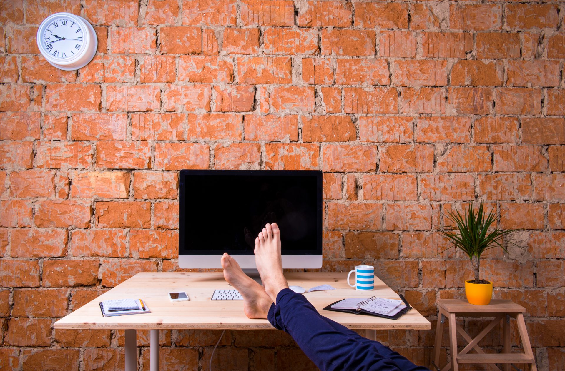 Feet of businessman, sitting at office desk, brick wall